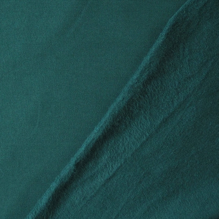 A close-up of a dark teal green fabric with a soft, plush texture, folded diagonally across the frame.