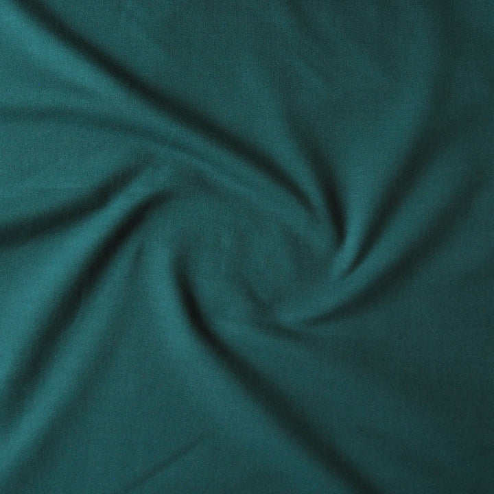 A close-up of dark teal green fabric with a soft, slightly textured surface, arranged in a gentle spiral drape.