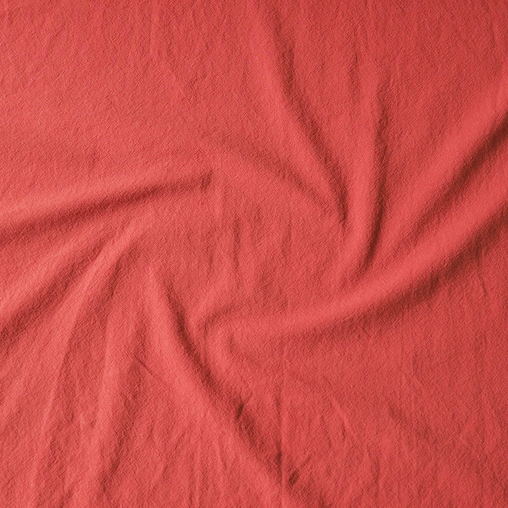 A close-up of textured fabric in a solid coral pink color, arranged with a central swirl of folds.