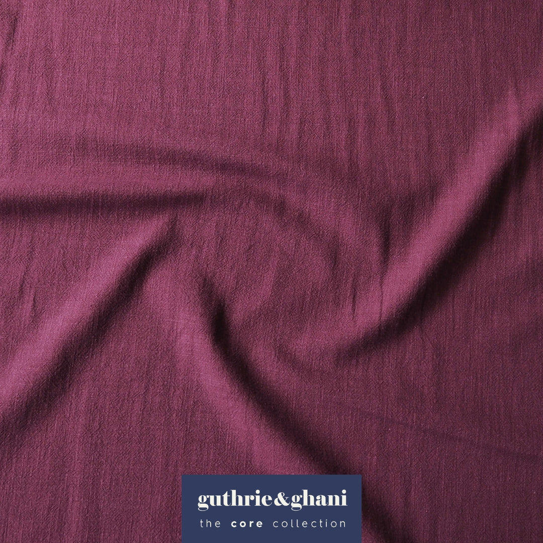 A close-up of draped mauve-purple fabric with a subtle crinkled texture, featuring a dark blue brand label at the bottom that reads 'guthrie&ghani the core collection'.