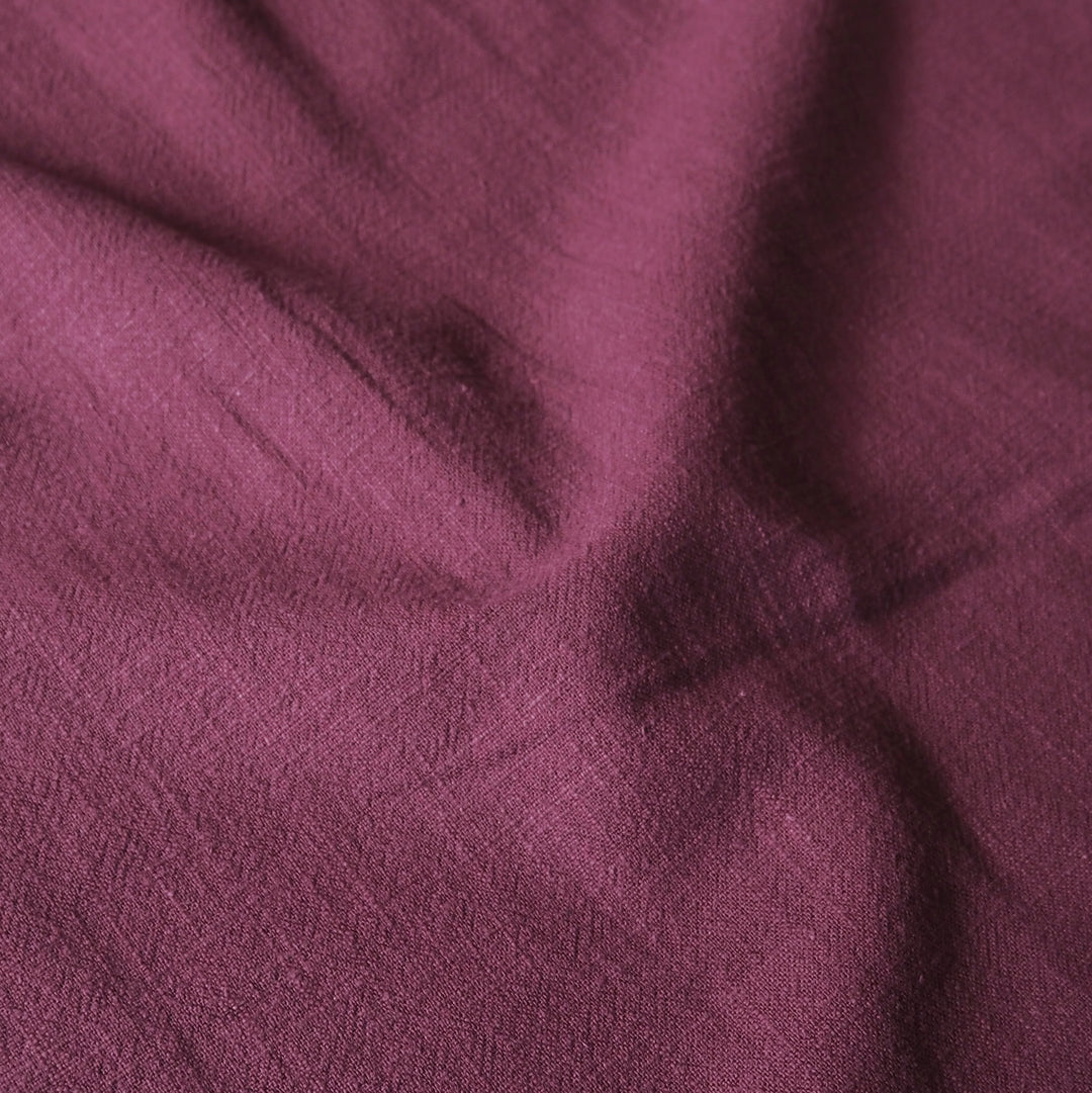 A close-up of draped fabric in a muted plum or burgundy-purple color, showing the textile texture and soft folds.
