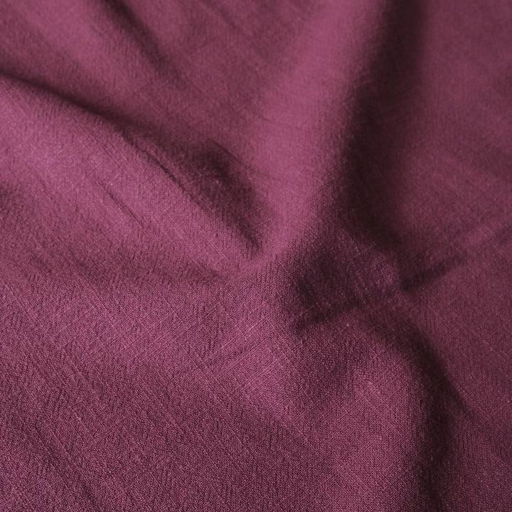 A close-up of draped fabric in a muted plum or burgundy-purple color, showing the textile texture and soft folds.