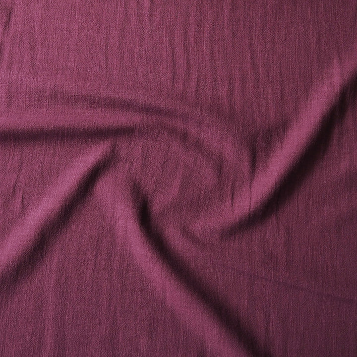 A close-up of draped mauve-purple fabric with a textured, slightly crinkled surface.