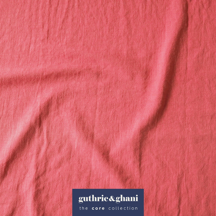 A close-up of textured pink fabric with soft folds and a dark blue brand label at the bottom reading 'guthrie&ghani the core collection'.