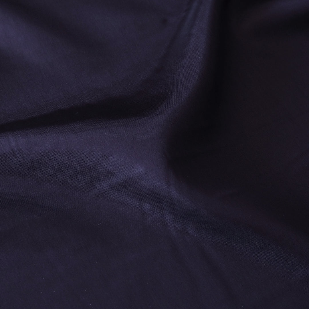 A close-up of dark navy blue fabric with soft folds and a smooth texture.