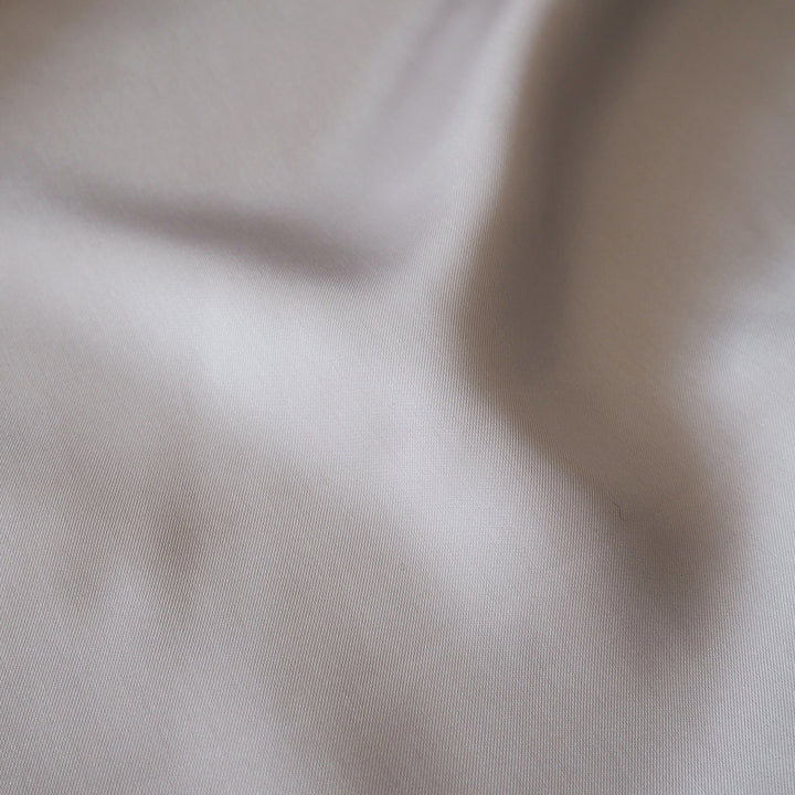 A close-up of draped light beige fabric with soft folds and a fine woven texture.