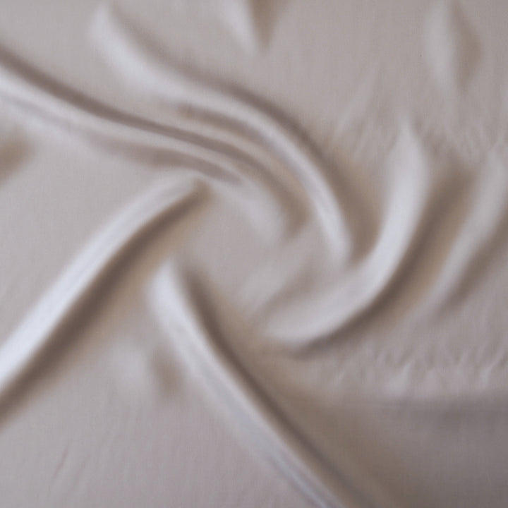 A close-up of draped off-white fabric with soft folds and a subtle sheen.
