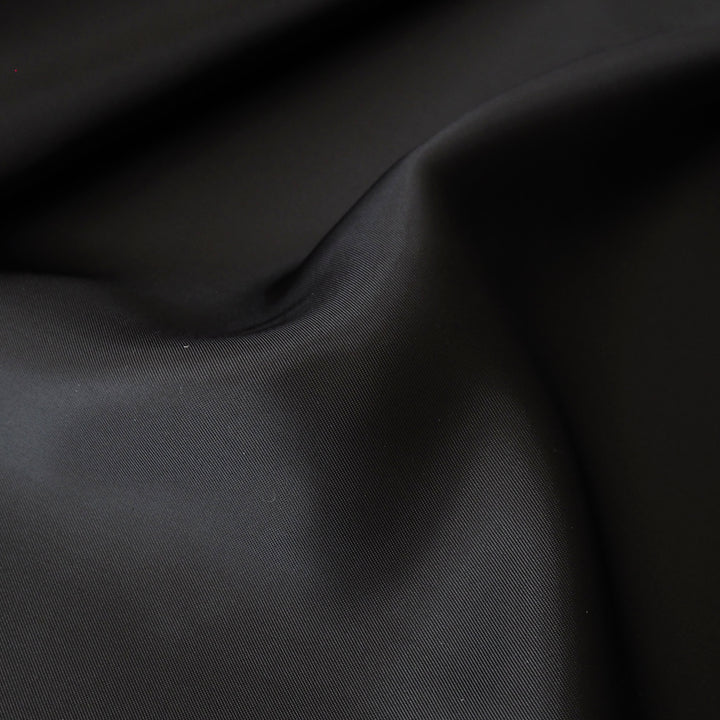 A close-up of draped black fabric with soft folds and a subtle sheen, showing the material texture and color.