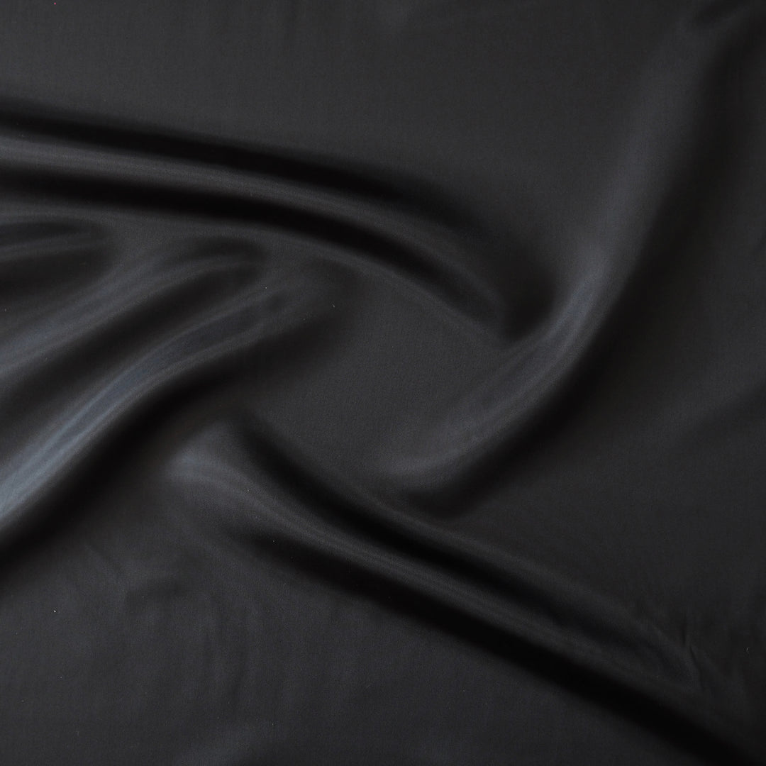 A close-up of draped black fabric with soft folds and a smooth texture.