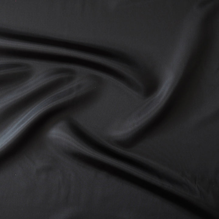 A close-up of draped black fabric with soft folds and a smooth texture.