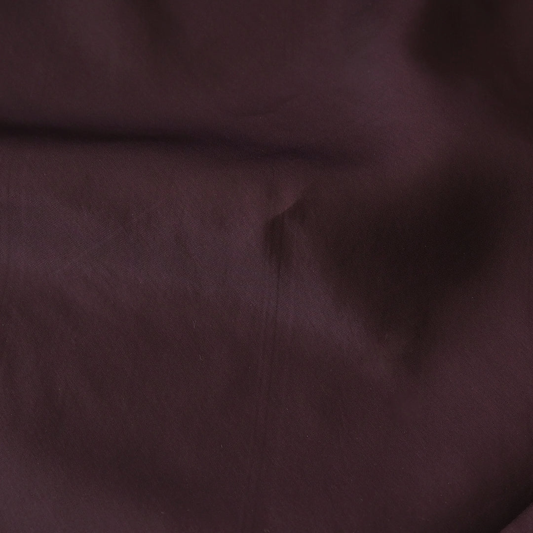 A close-up of dark plum purple fabric with soft folds and a subtle sheen.