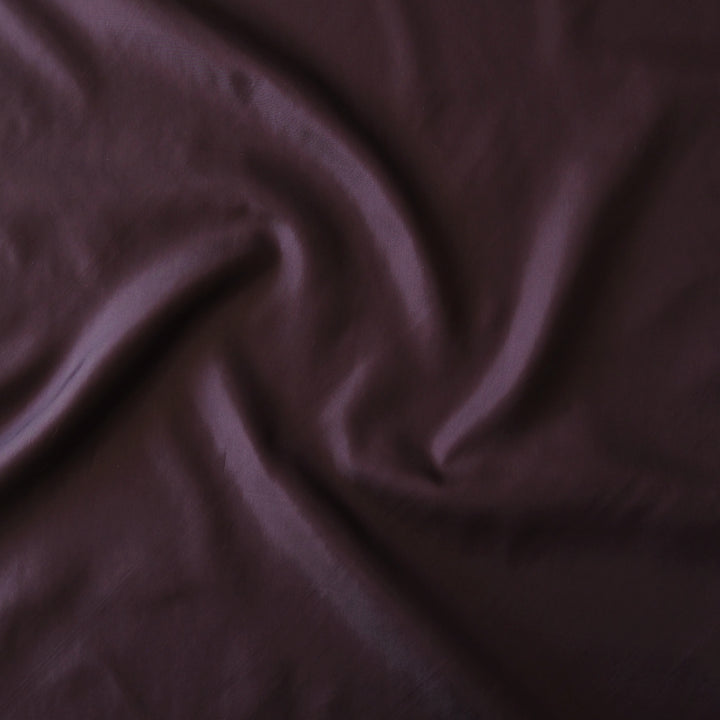 A close-up of draped dark plum purple fabric with soft folds and a smooth texture.