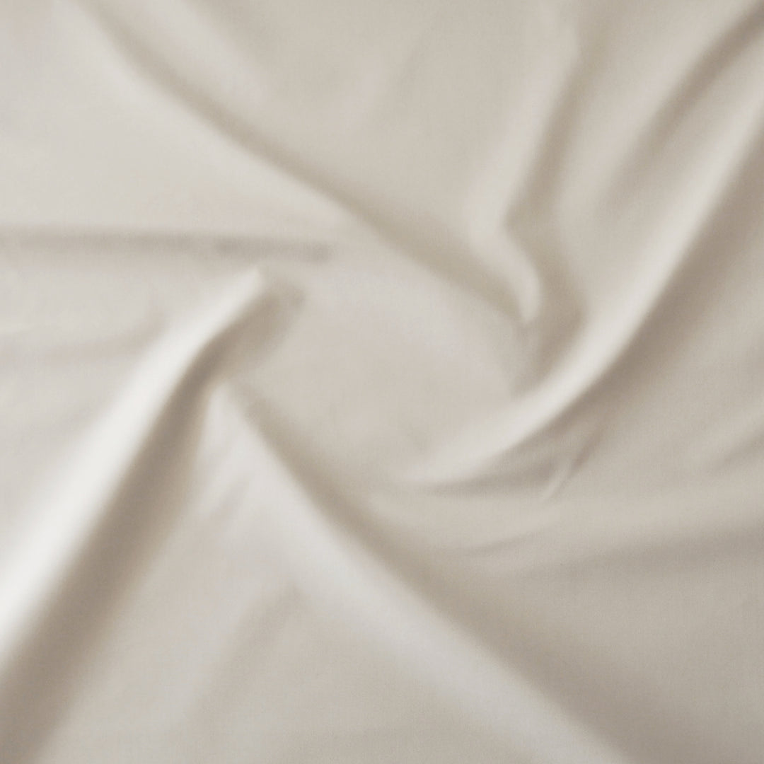 A close-up of draped beige fabric with soft folds and a smooth texture.