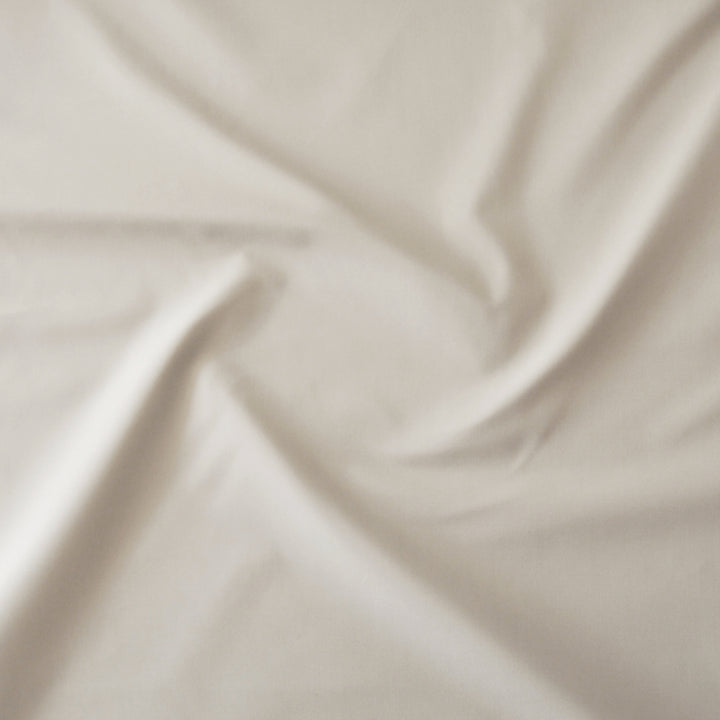 A close-up of draped beige fabric with soft folds and a smooth texture.