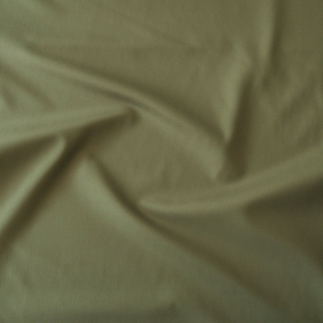 A close-up of draped olive green fabric with soft folds and a smooth texture.