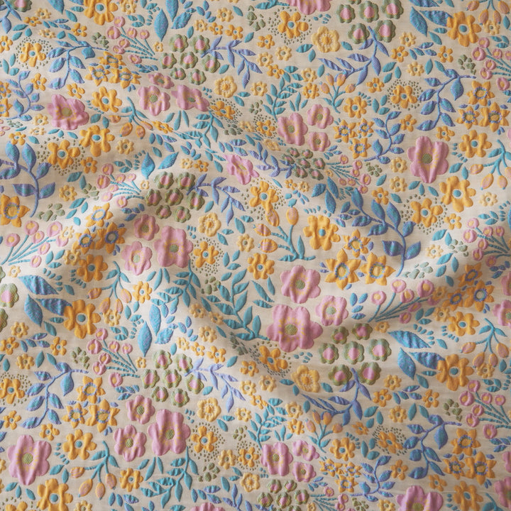 A close-up of a fabric with a dense, multi-colored floral pattern featuring pink, yellow, and blue flowers on a cream background.