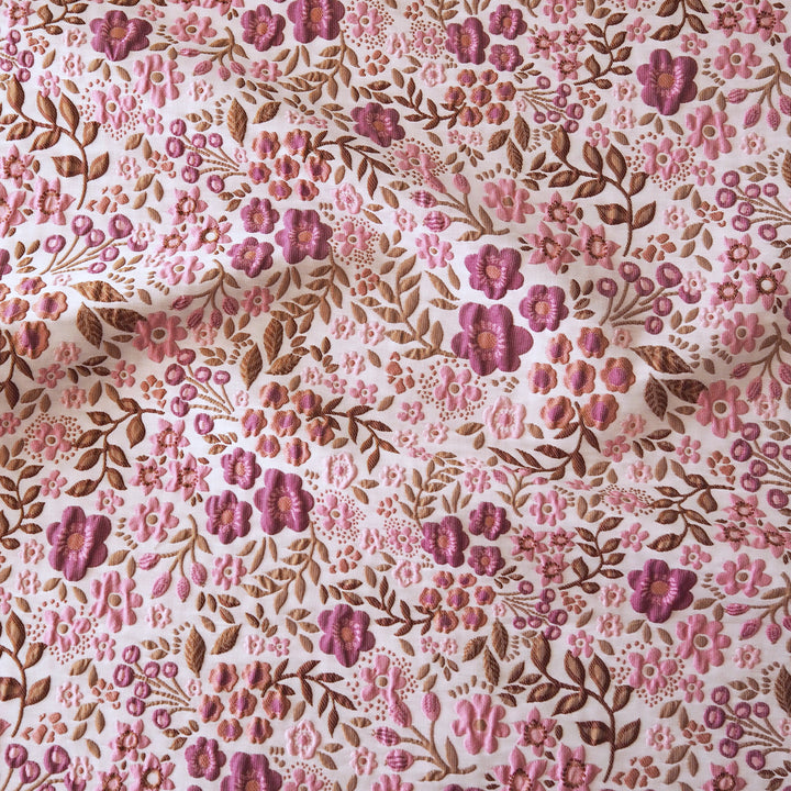 A close-up of a floral fabric with a dense pattern of pink and purple flowers and brown leaves on a white background.