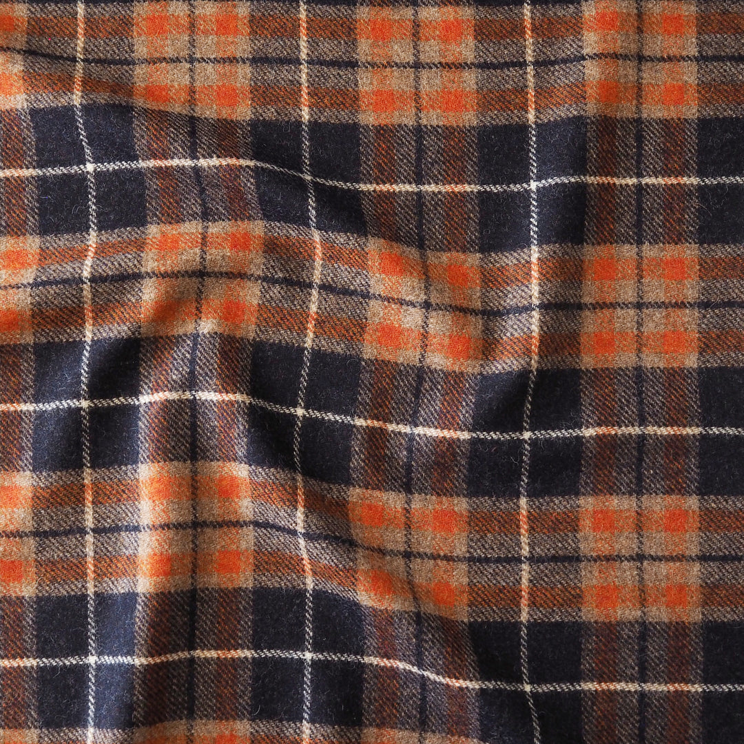 A close-up of a plaid fabric pattern with dark navy blue, orange, beige, and thin white intersecting lines.
