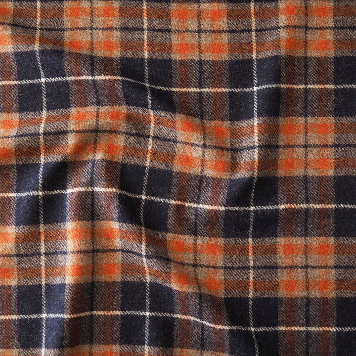 A close-up of a plaid fabric pattern with dark navy blue, orange, beige, and thin white intersecting lines.