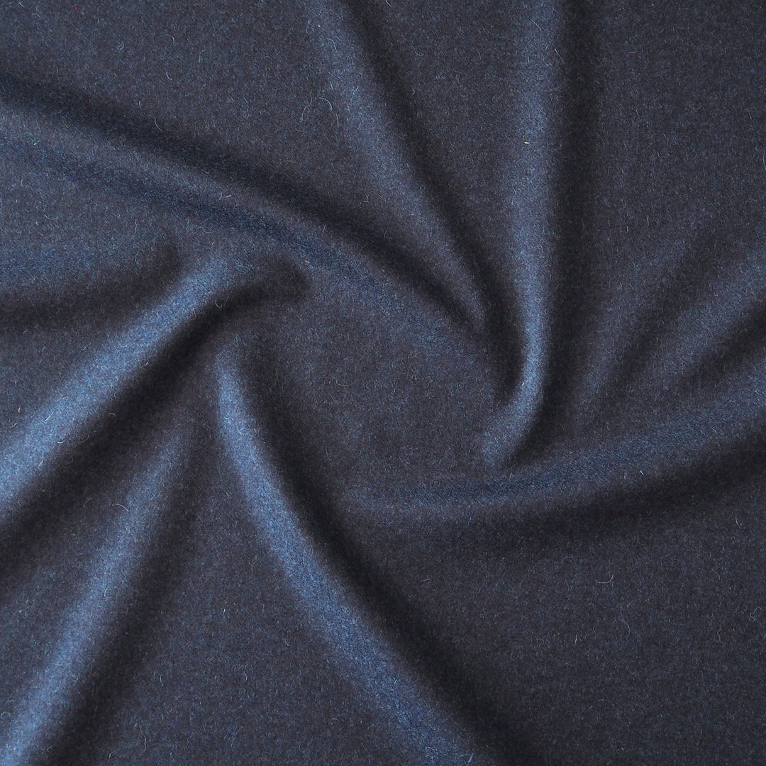 A close-up of dark navy blue fabric with a soft, slightly fuzzy texture, arranged in a central swirl pattern.