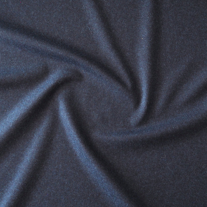 A close-up of dark navy blue fabric with a soft, slightly fuzzy texture, arranged in a central swirl pattern.