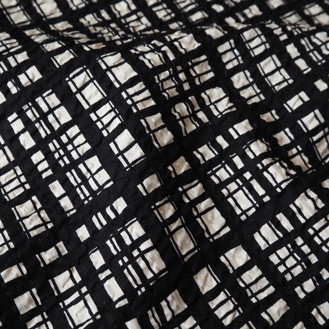 A close-up of a black and off-white quilted fabric with a hand-drawn grid plaid pattern.