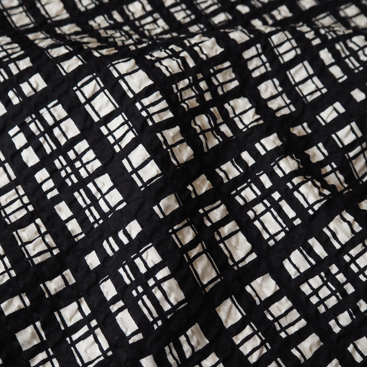 A close-up of a black and off-white quilted fabric with a hand-drawn grid plaid pattern.