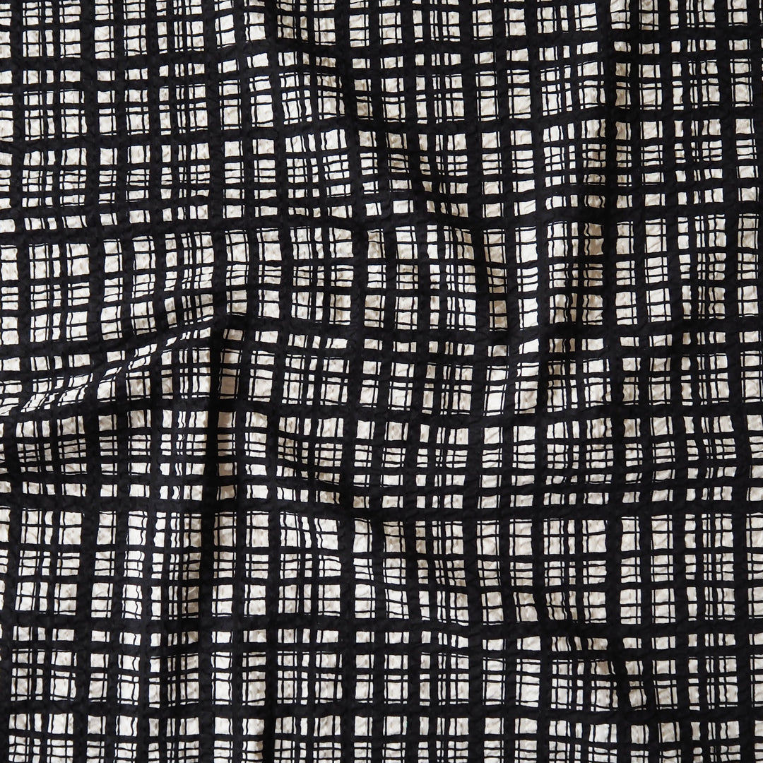 A close-up of a black and off-white woven fabric with a textured, hand-drawn plaid pattern.