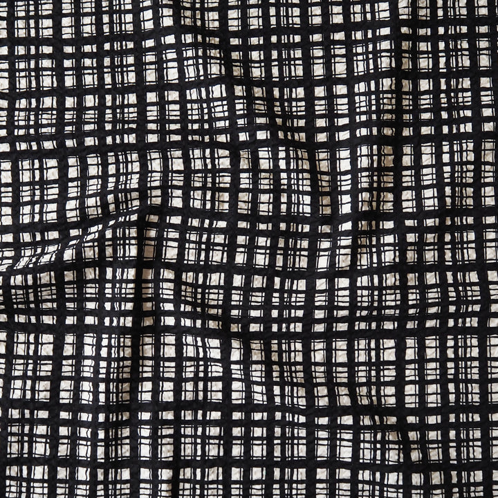 A close-up of a black and off-white woven fabric with a textured, hand-drawn plaid pattern.