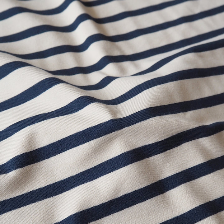 Close-up of a striped fabric with alternating navy blue and off-white horizontal stripes, showing soft folds and texture.