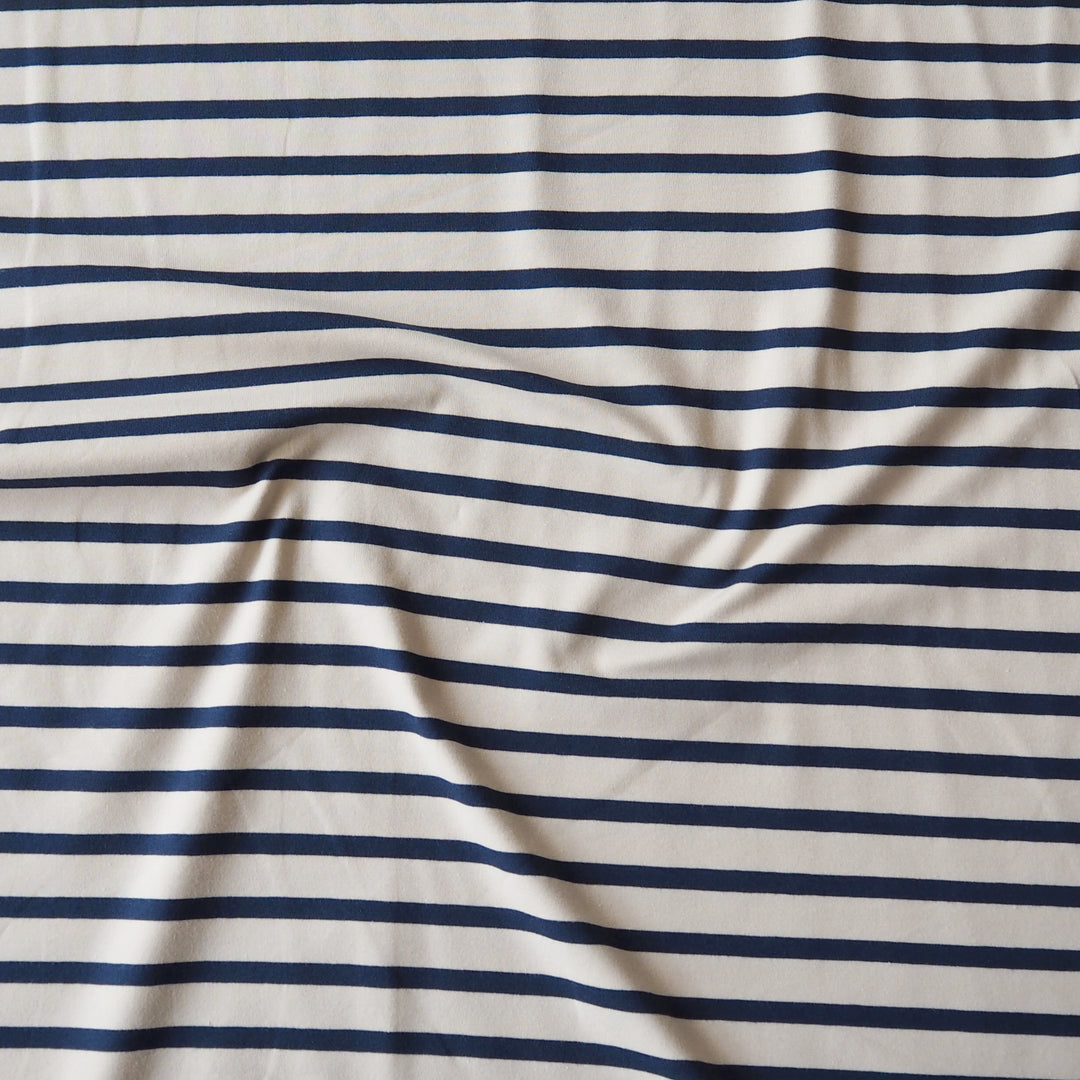 A close-up of a striped fabric with horizontal navy blue stripes on an off-white background, showing soft folds and wrinkles.