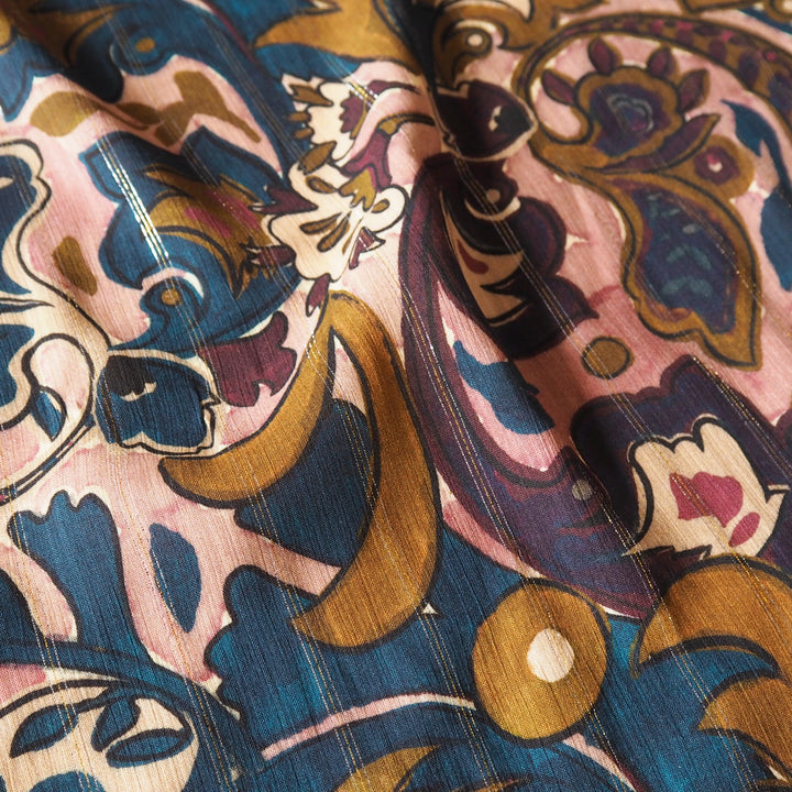 A close-up of patterned fabric with an ornate paisley and floral design in dusty pink, deep blue, mustard gold, and dark purple.