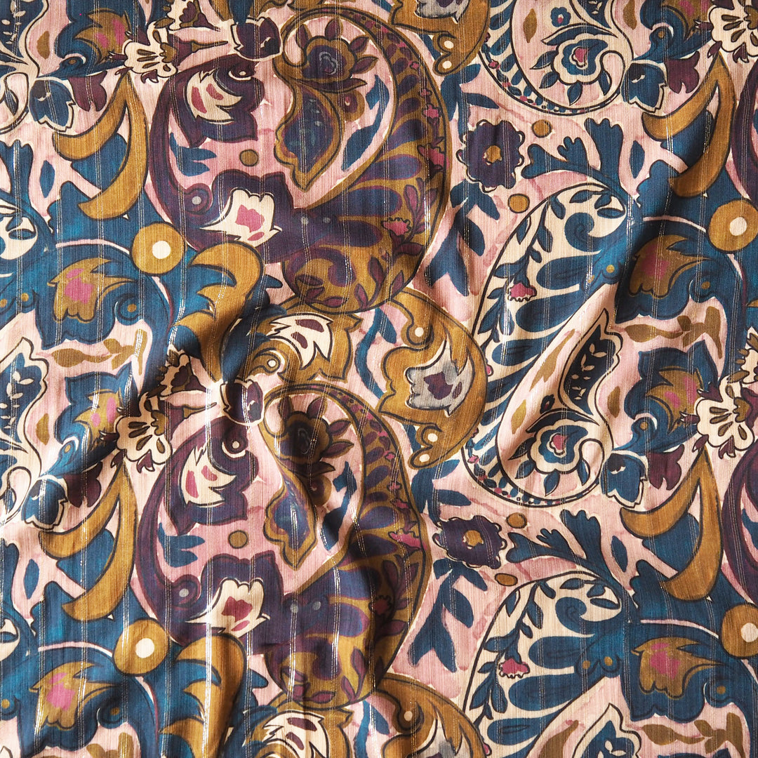 A close-up of a draped fabric with an intricate paisley and floral pattern in dusty pink, navy blue, ochre gold, and cream.