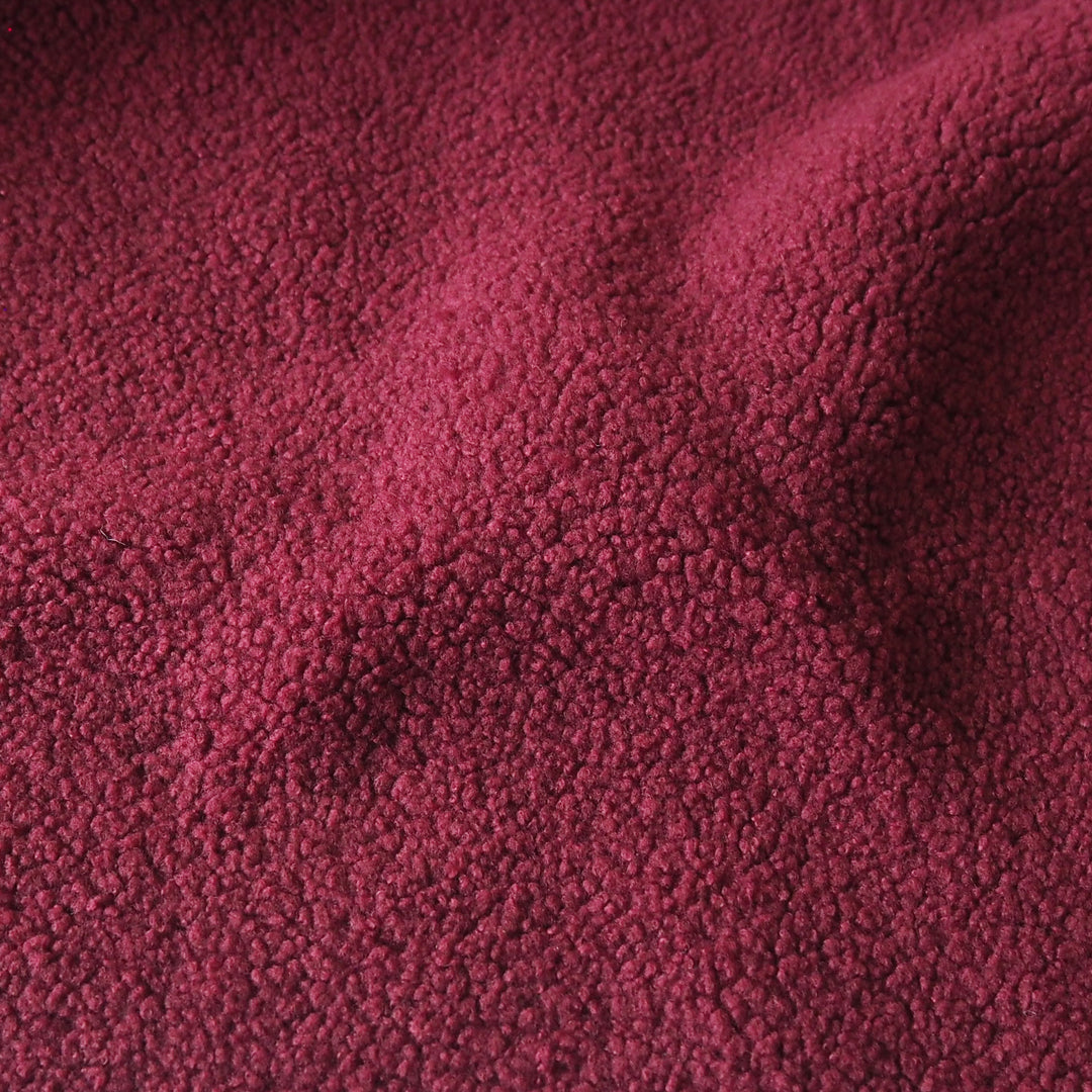 A close-up of textured fleece fabric in a deep burgundy pink color, showing the soft, looped pile texture with gentle folds.