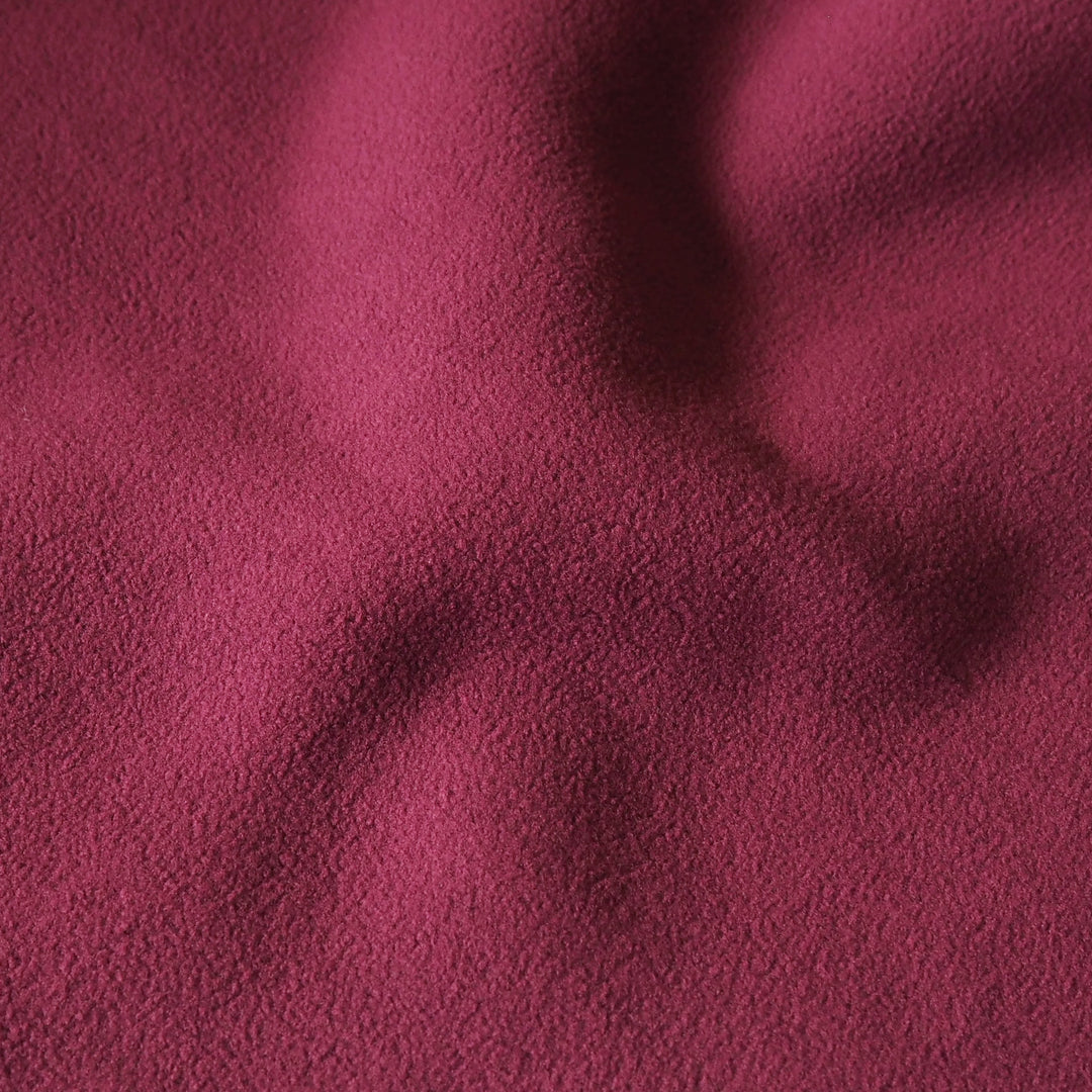 A close-up of textured fabric in a deep red color, showing soft folds and shadows across the surface.