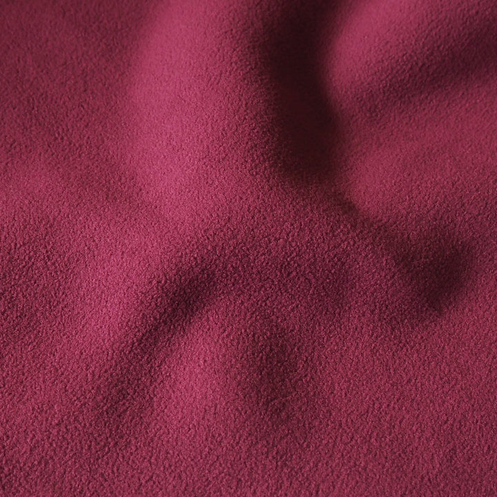 A close-up of textured fabric in a deep red color, showing soft folds and shadows across the surface.