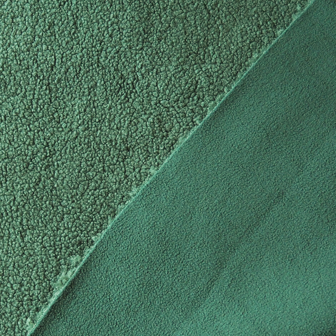 A close-up of a green textured fabric, showing two different pile directions: a short-pile bouclé texture on the left and a smoother microfiber or fleece texture on the bottom right, divided by a diagonal seam.