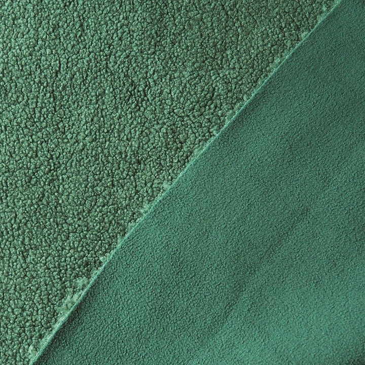 A close-up of a green textured fabric, showing two different pile directions: a short-pile bouclé texture on the left and a smoother microfiber or fleece texture on the bottom right, divided by a diagonal seam.