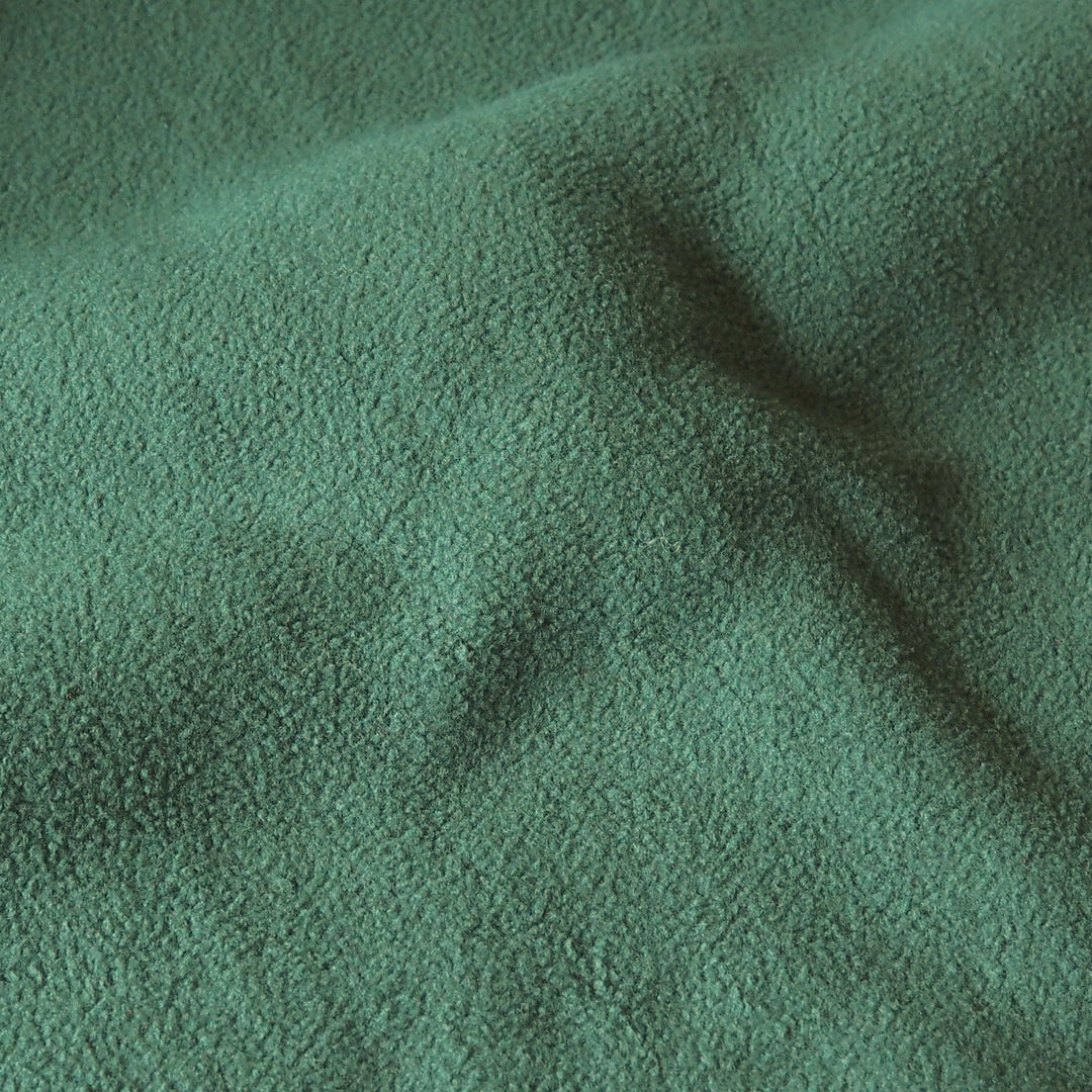 A close-up of textured green fabric with soft folds and a slightly plush or bouclé surface.