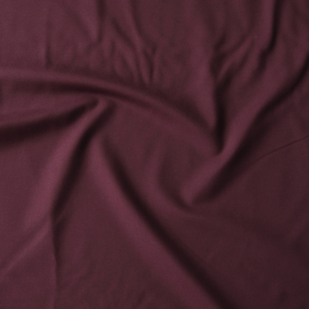 A close-up of draped burgundy fabric with soft folds and a smooth texture.
