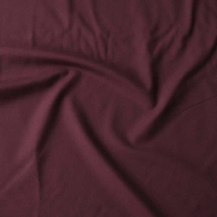 A close-up of draped burgundy fabric with soft folds and a smooth texture.