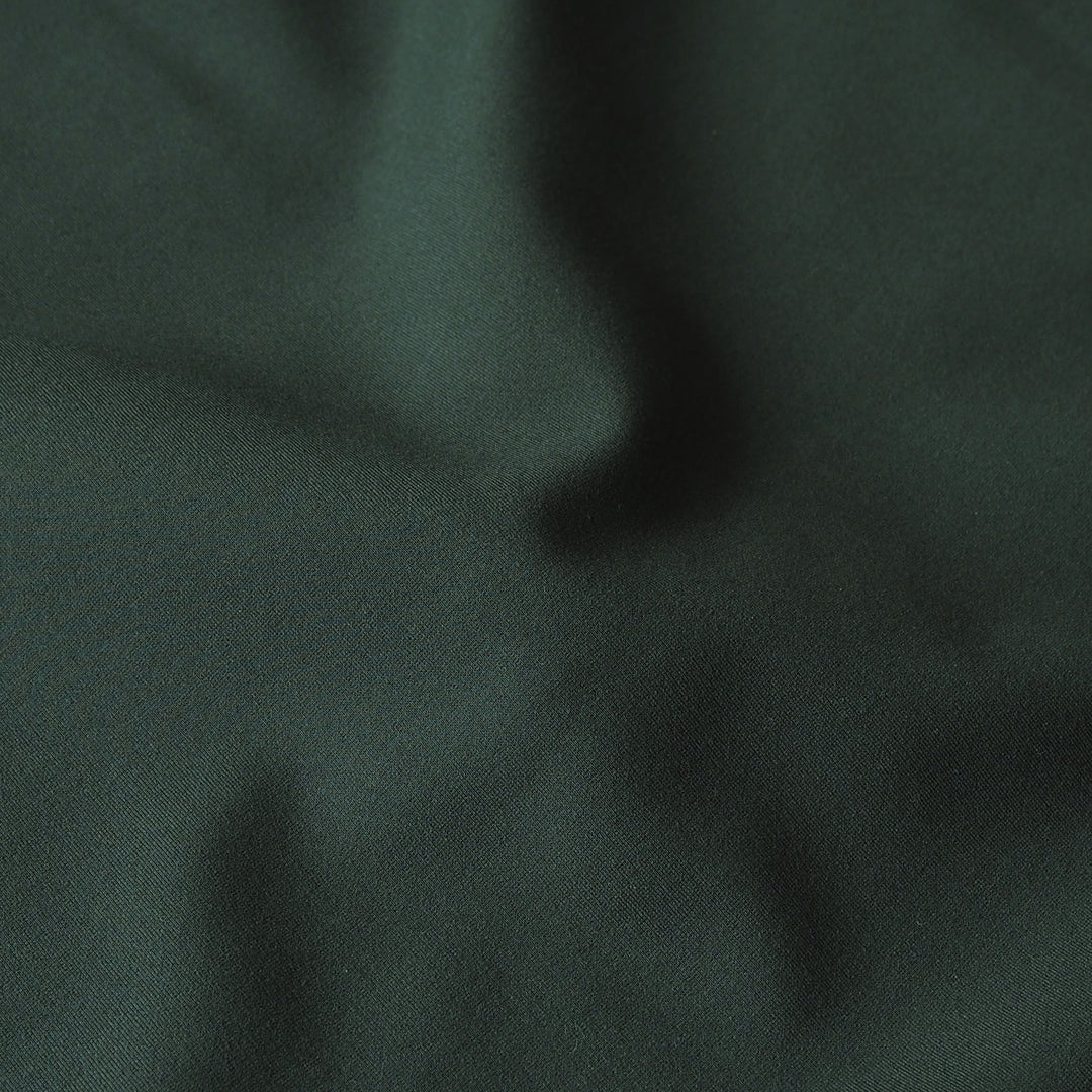 A close-up of dark forest green fabric with soft folds and a slightly textured surface.