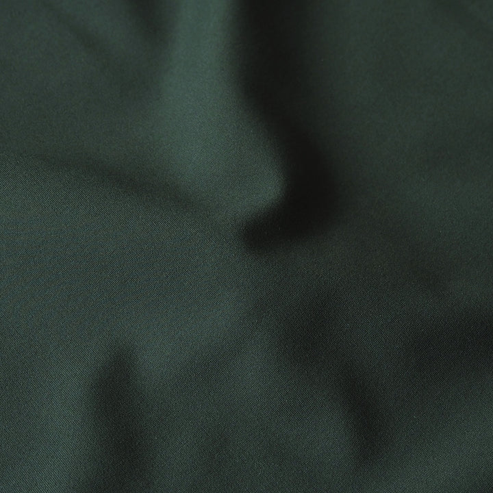A close-up of dark forest green fabric with soft folds and a slightly textured surface.