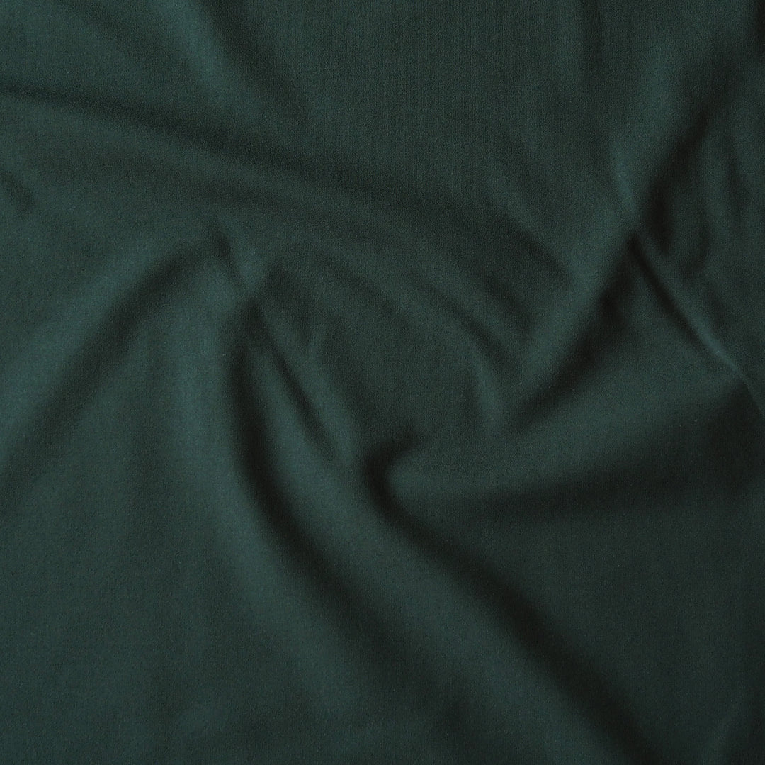 Dark forest green fabric with soft folds and a smooth texture filling the frame.