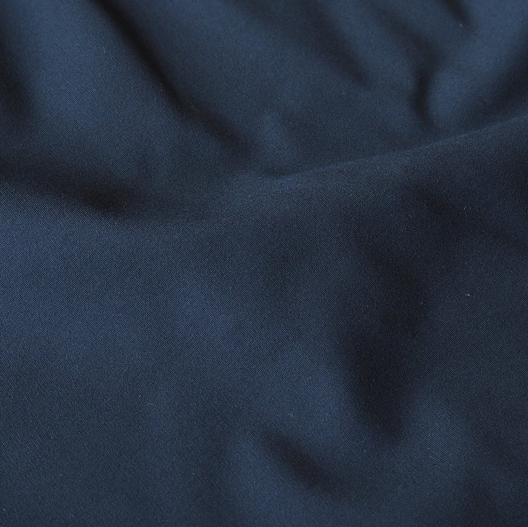 A close-up of dark navy blue fabric with soft folds and a smooth texture.