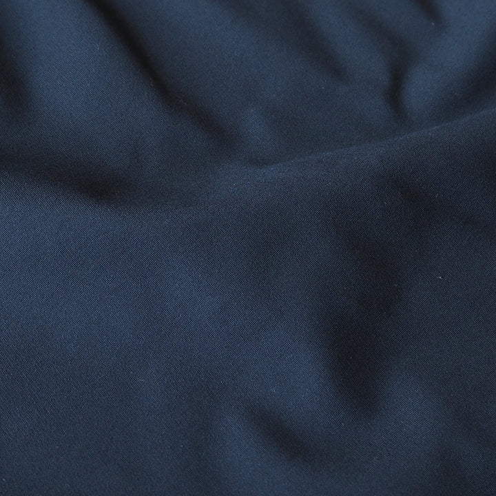 A close-up of dark navy blue fabric with soft folds and a smooth texture.