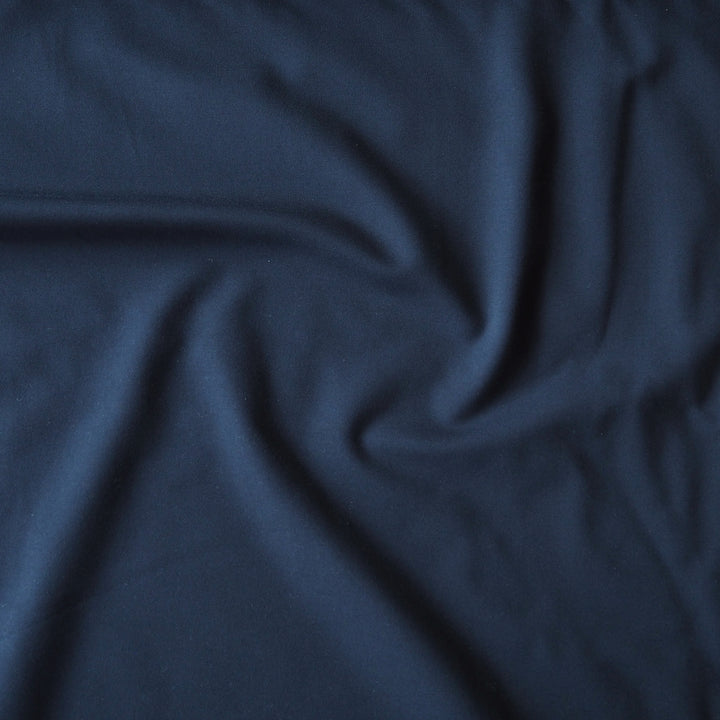 A close-up of draped navy blue fabric with soft folds and a smooth texture.