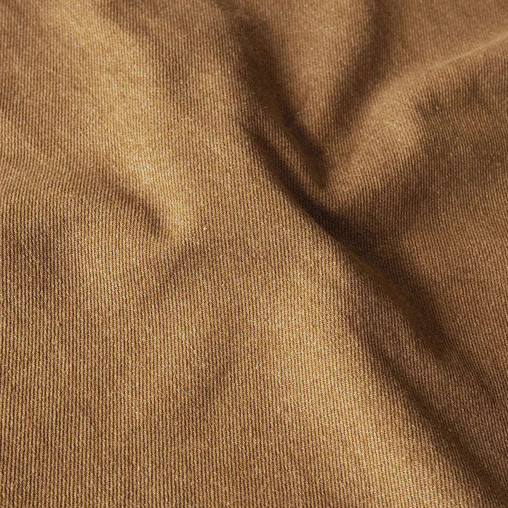 A close-up of draped brown denim fabric with a fine twill texture and soft shadows in the folds.