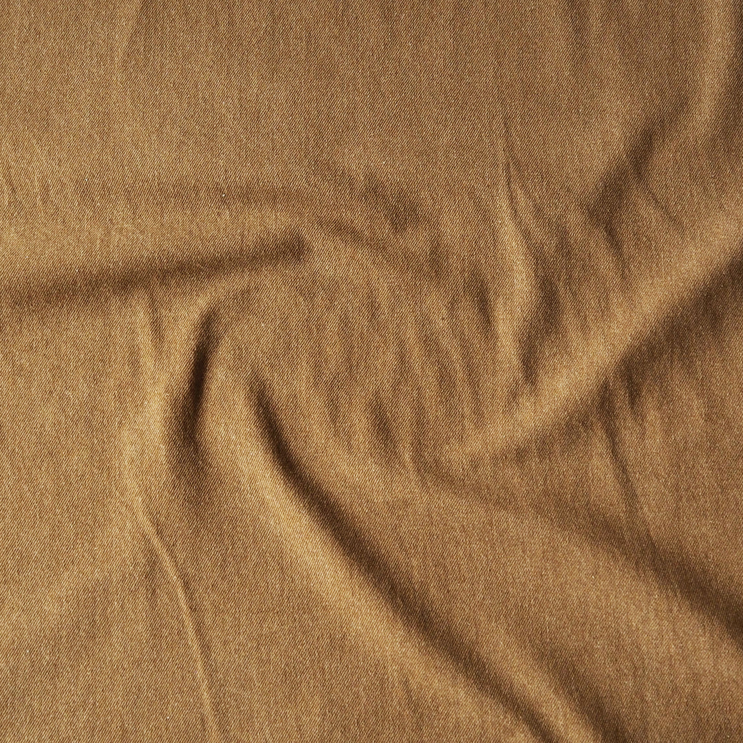 A close-up of draped camel brown denim fabric with a soft, textured surface.