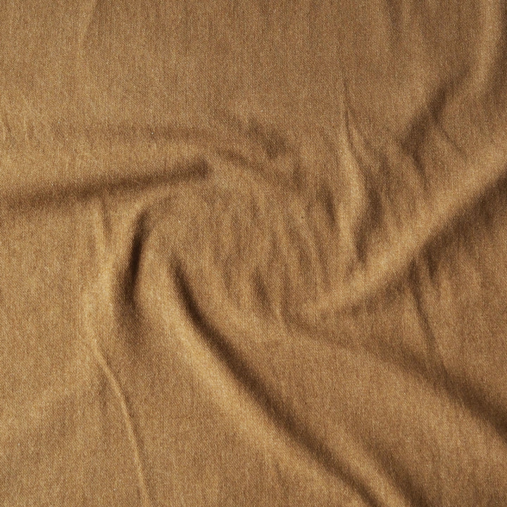 A close-up of draped camel brown denim fabric with a soft, textured surface.